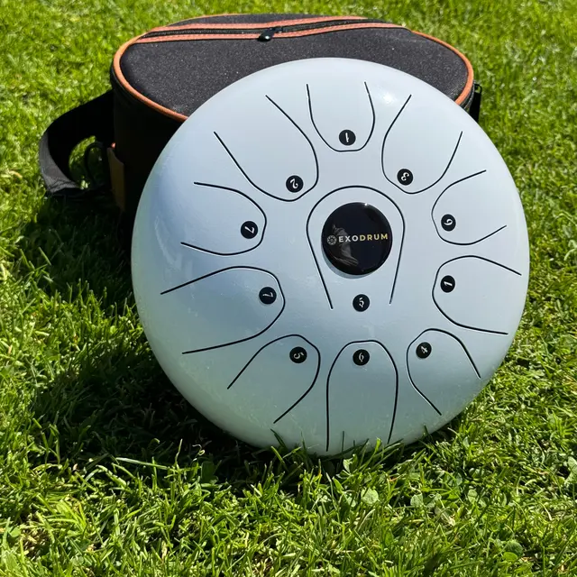 Tongue drum Exodrum Harmony blanc posé dans l’herbe devant sa housse